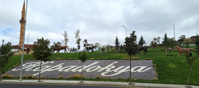 Skulpture konj in napis Kapadokija ob cesti z minaretom v ozadju.